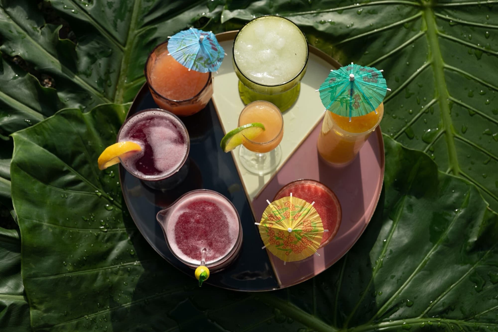 Frozen tropical cocktails with paper umbrellas on a tray of palm leaves